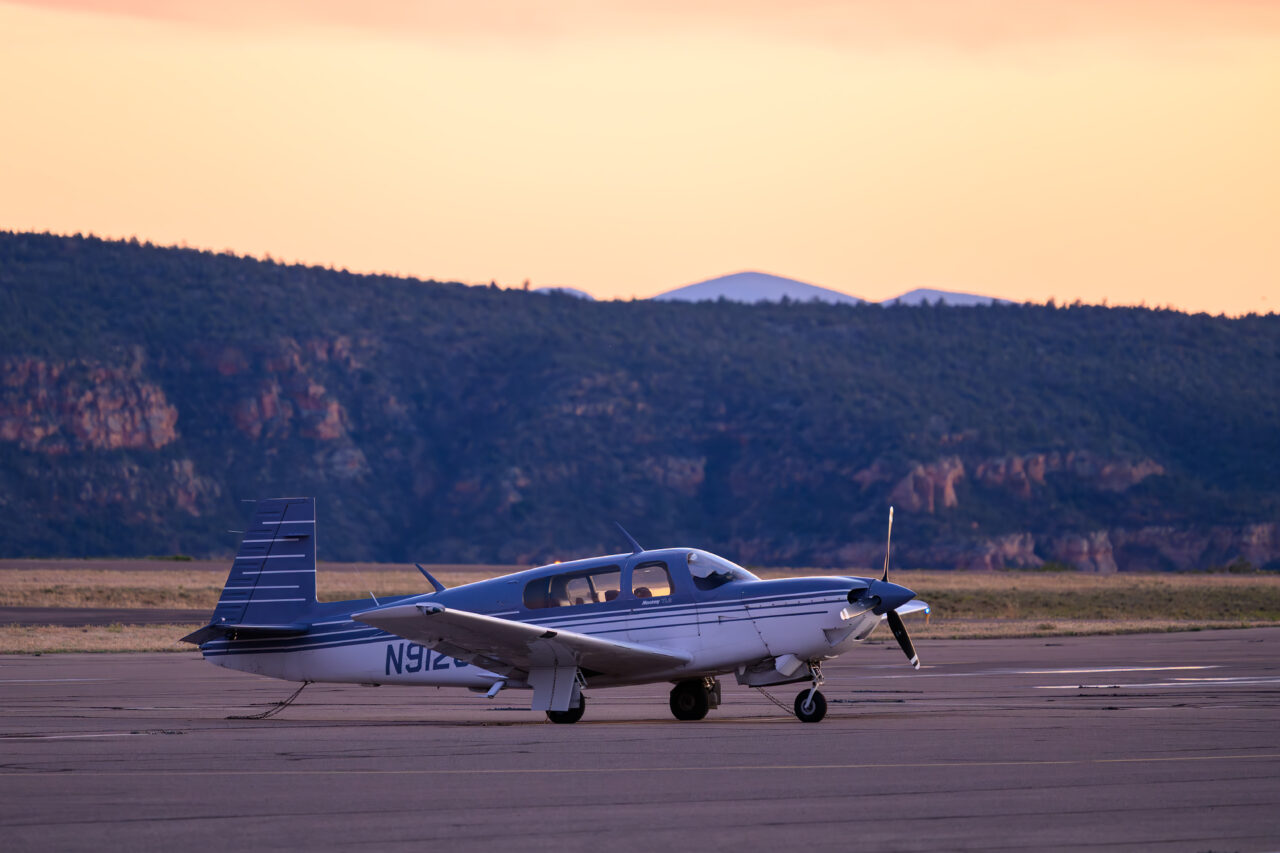 A small blue and white propeller plane parked on the quiet Sedona Airport tarmac at dusk.