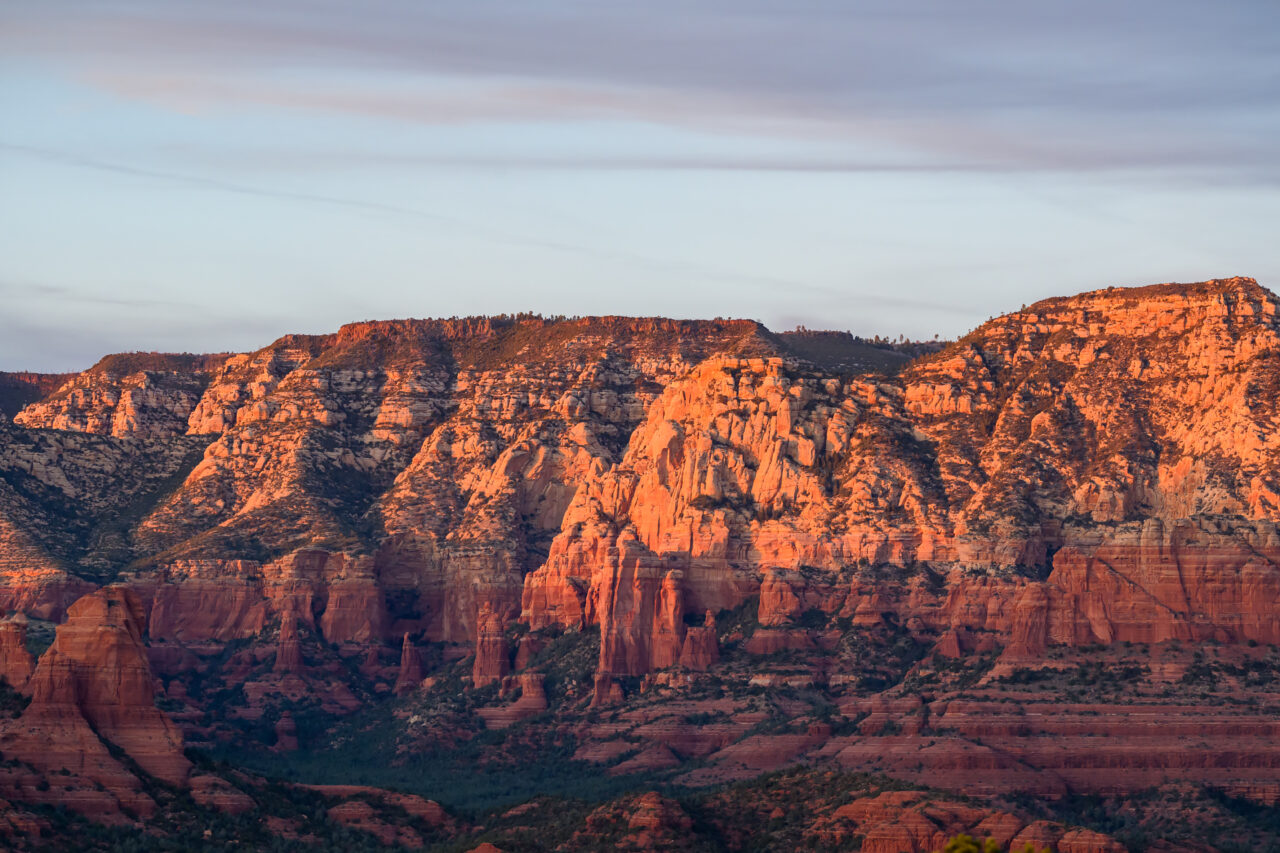 Close-up of rugged red rock cliffs in Sedona bathed in warm, late-afternoon sunlight.