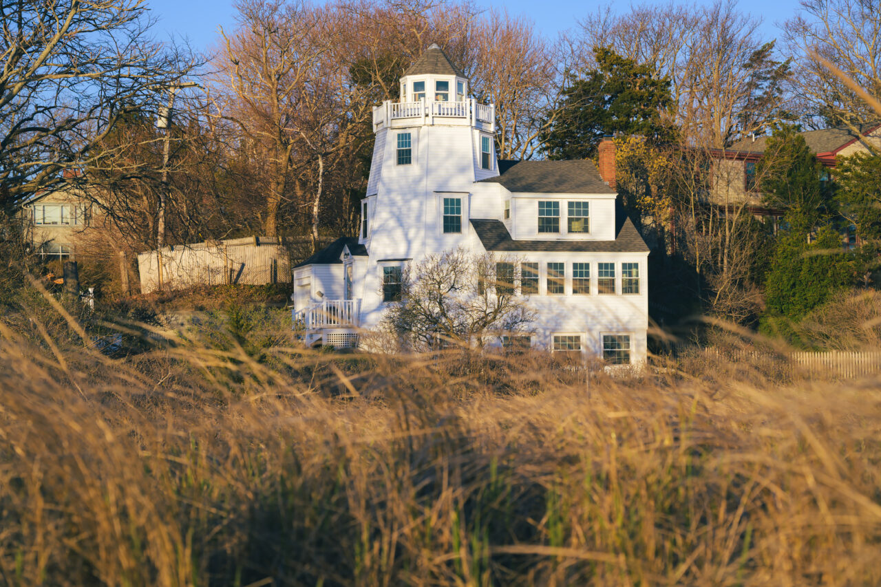 Lighthouse-style house along Powder Point Bridge in Duxbury in golden morning light.