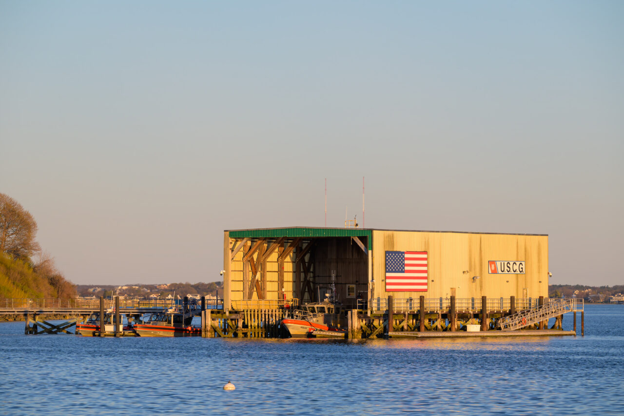 The U.S. Coast Guard station at Hull glows in warm evening light from across the water.
