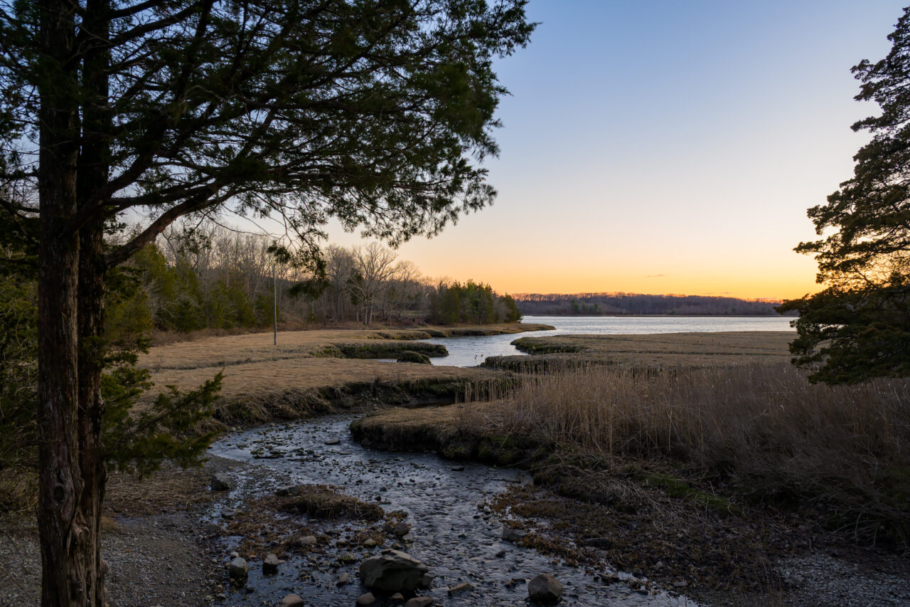 A wide view of the winding creek and salt marsh at Bare Cove Park in Weymouth under a clear sunset sky.