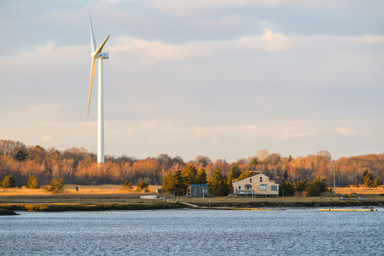 Wind turbine rising above a marsh and waterfront home at Damon's Point.