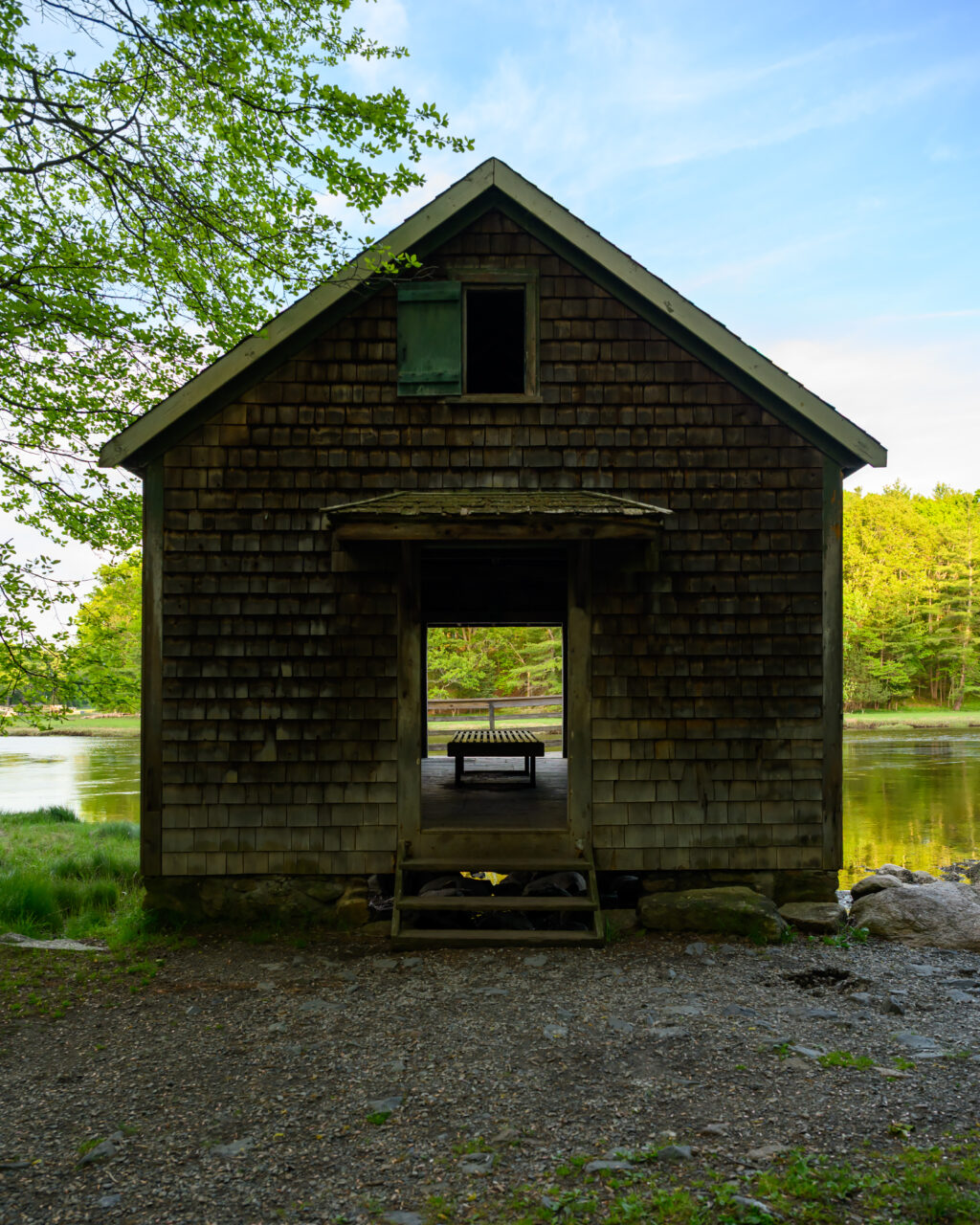 A symmetrical, straight-on look at the weathered shingle boathouse sitting over the river at Norris Reservation in Norwell.