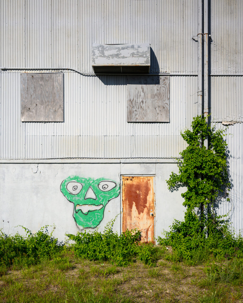Green graffiti face and rusty door on an abandoned building at South Weymouth Naval Air Station.