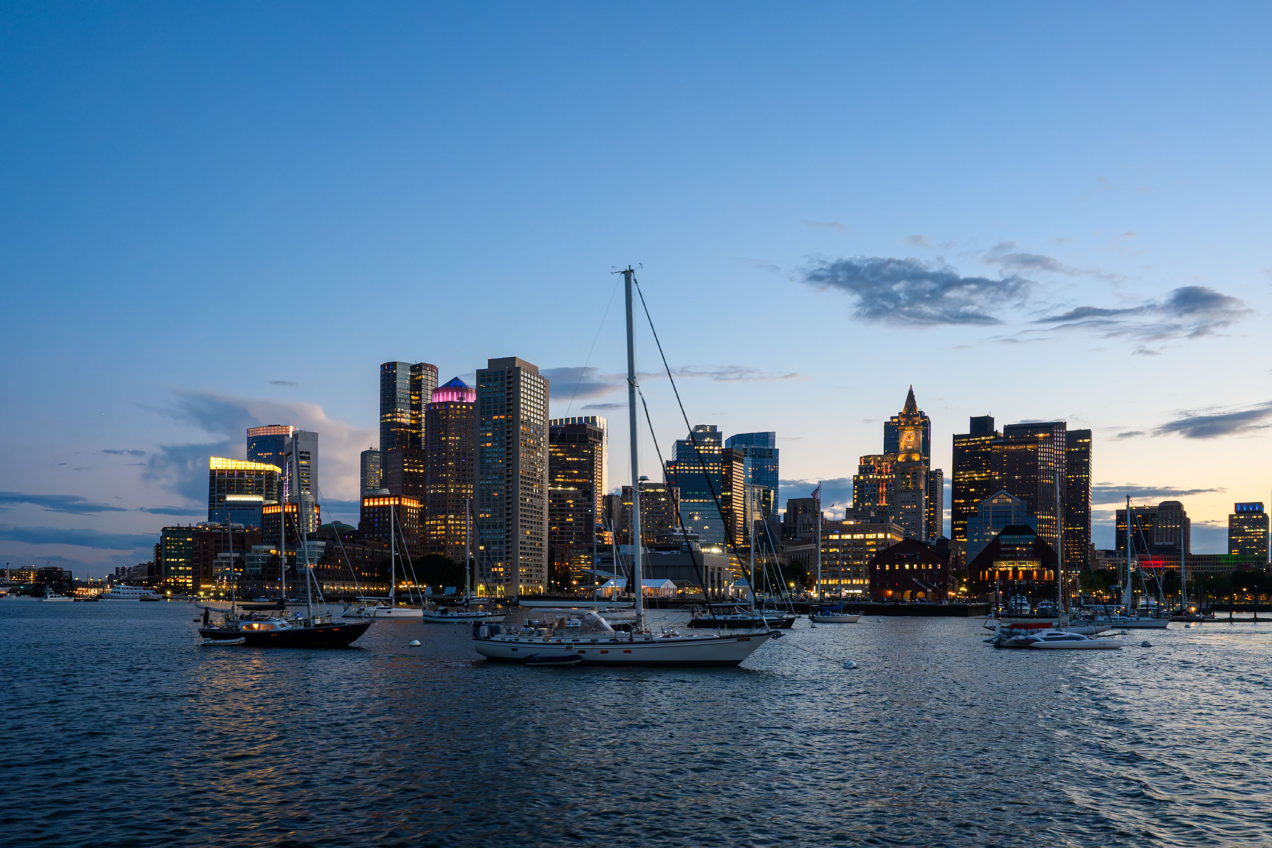The view from a ferry ridge from Boston with sailboats anchored in the harbor at blue hour.