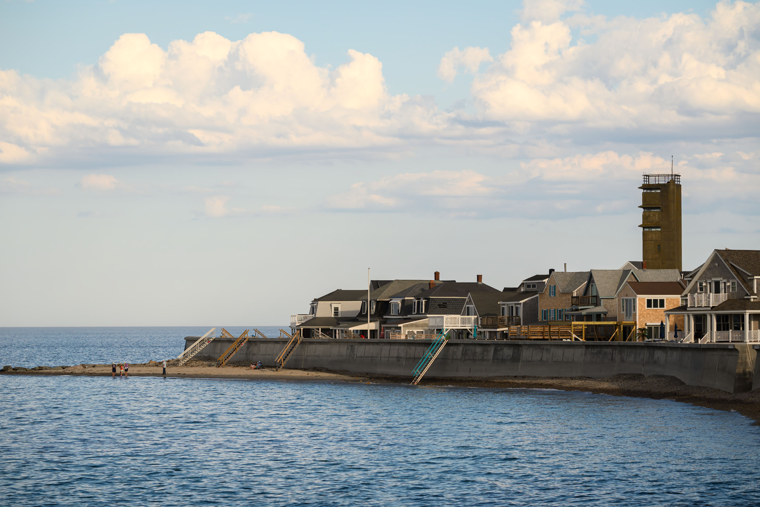 Brant Rock seawall in Marshfield, with the tower and waterfront homes viewed from the beach.