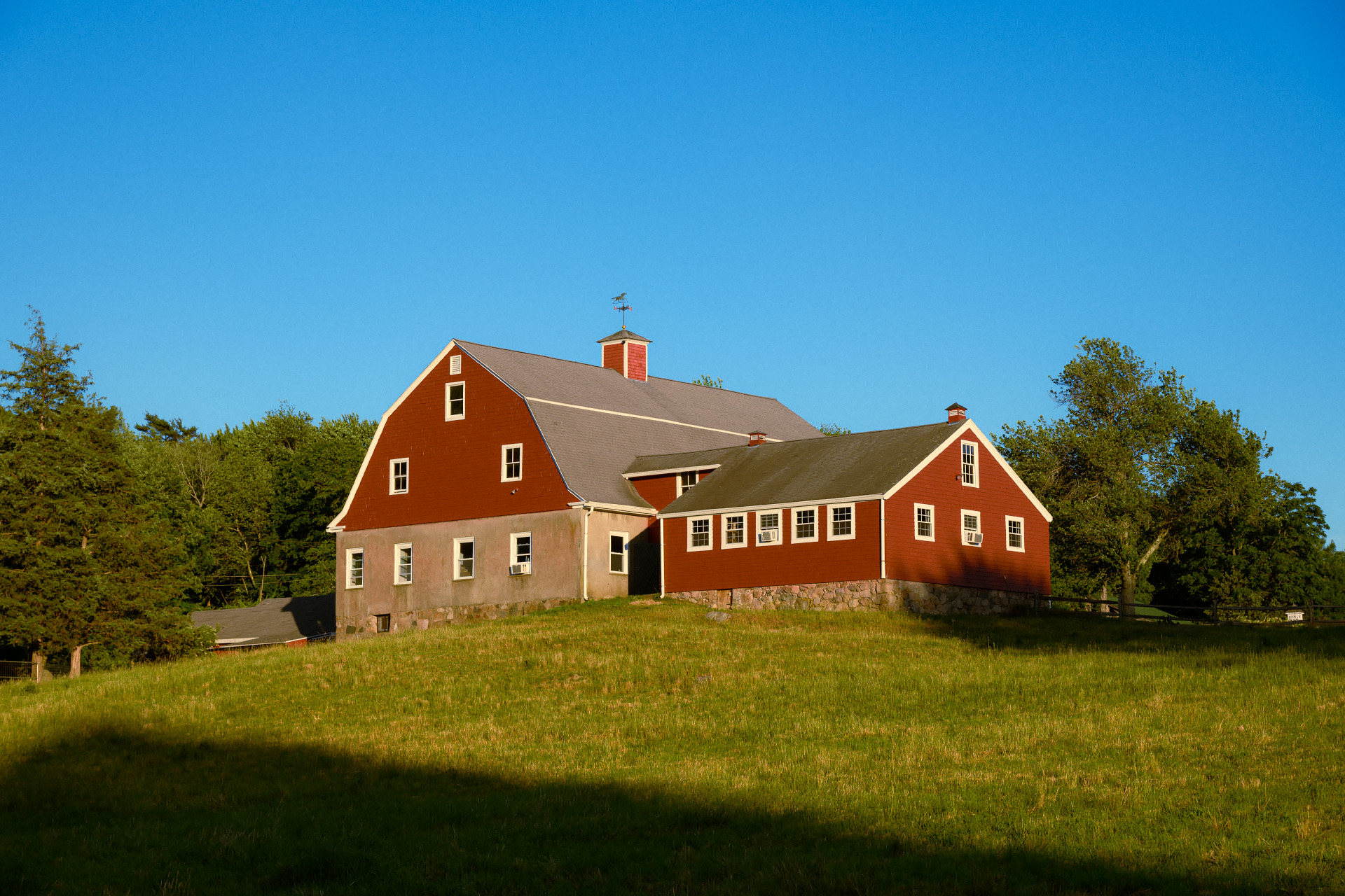 Large red gambrel barn at Weir River Farm on a hill in golden hour light, Hingham MA.