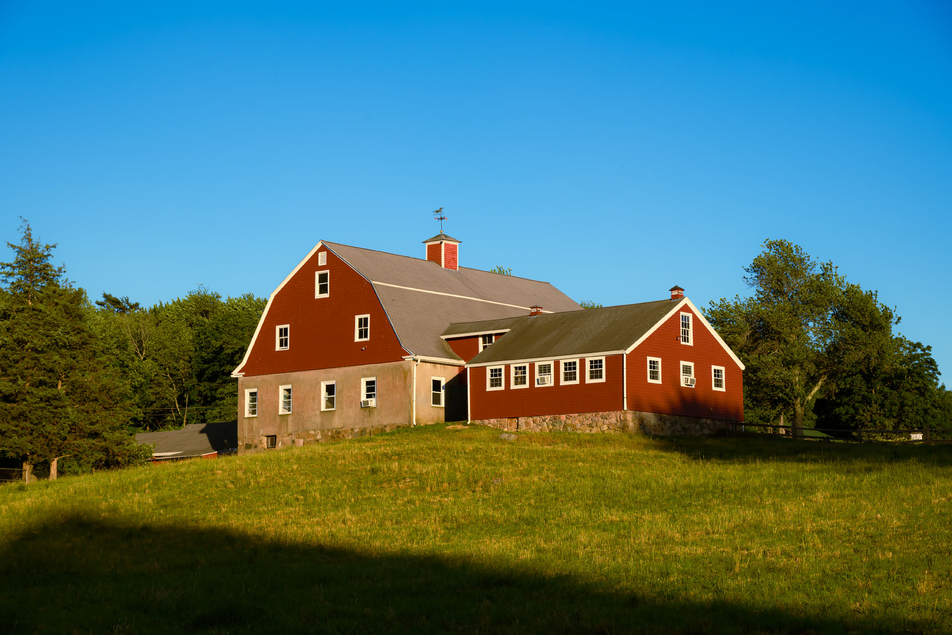 Large red gambrel barn at Weir River Farm on a hill in golden hour light, Hingham MA.