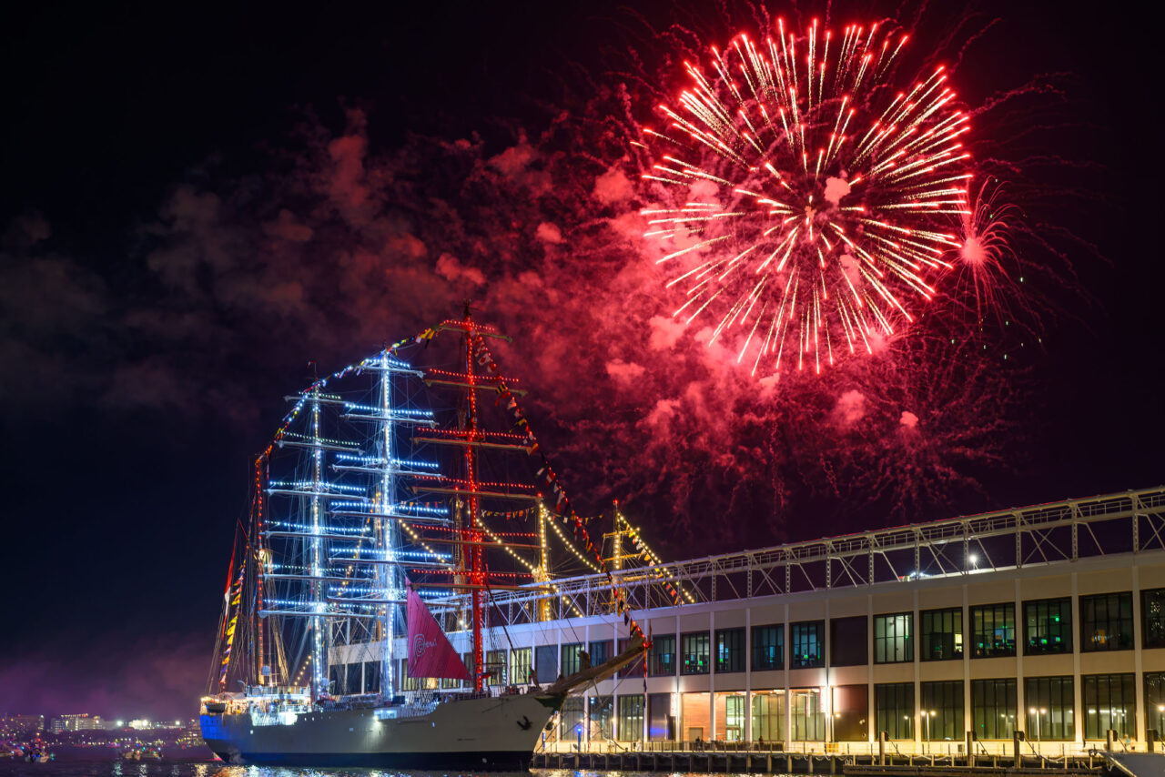 Red fireworks exploding above Boston Harbor during Sail Boston 2026.